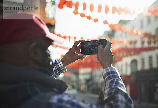 Männlicher Tourist mit Fotohandy beim Fotografieren von Papierlaternen in der Stadt