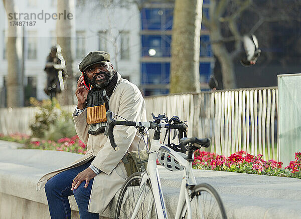 Geschäftsmann mit Fahrrad  der im Stadtpark mit seinem Smartphone telefoniert