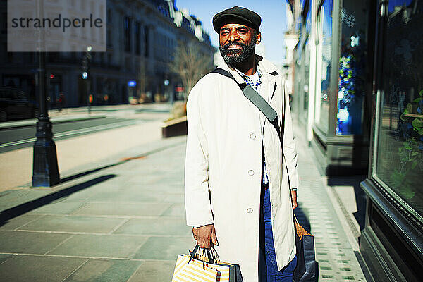 Gut aussehender Mann mit Einkaufstüten vor einem sonnigen städtischen Geschäft