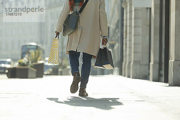 Mann mit Einkaufstaschen auf dem sonnigen Bürgersteig der Stadt