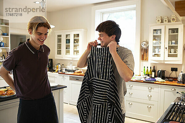 Glückliche Teenager mit Schürze beim Kochen in der Küche