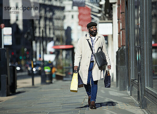 Geschäftsmann mit Einkaufstüten auf einem sonnigen Bürgersteig in der Stadt