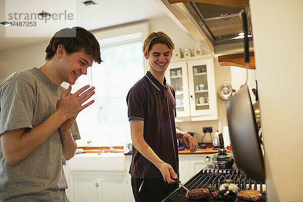 Glückliche Teenager-Jungs grillen Hamburger am Küchenherd