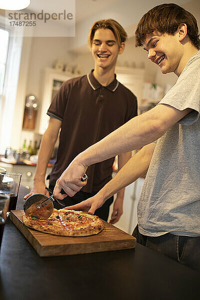 Fröhliche Teenager-Jungs schneiden frische Pizza in der Küche