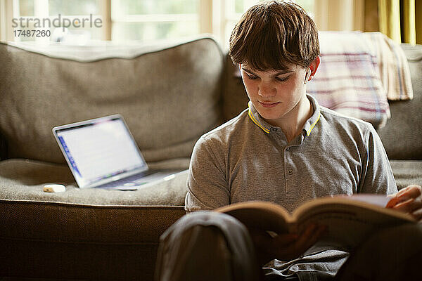 Konzentrierter Teenager mit Lehrbuch beim Lernen zu Hause