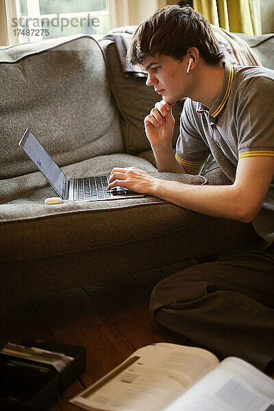 Konzentrierter Teenager  der im Wohnzimmer am Laptop lernt