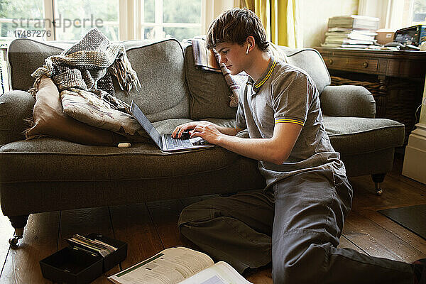 Konzentrierter Jugendlicher mit Laptop  der im Wohnzimmer zu Hause lernt