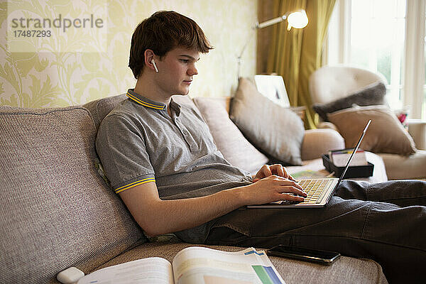 Jugendlicher mit Ohrstöpseln und Laptop auf dem Wohnzimmersofa