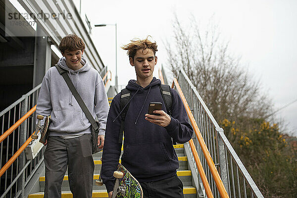 Jugendliche mit Skateboard und Smartphone steigen eine Treppe hinunter