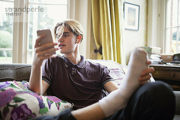 Teenager  der sein Smartphone auf dem Wohnzimmersofa benutzt