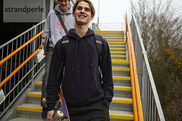 Fröhlicher Teenager mit Skateboard  der eine städtische Treppe hinunterfährt