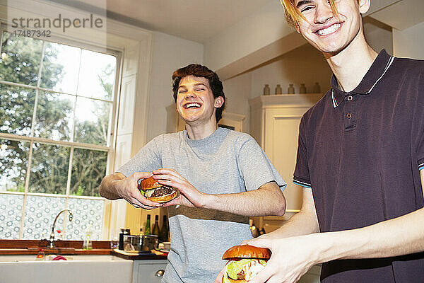 Porträt glücklicher Teenager-Jungs  die in der Küche Hamburger essen
