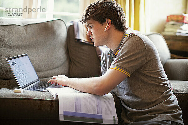 Konzentrierter Jugendlicher mit Laptop bei den Hausaufgaben im Wohnzimmer