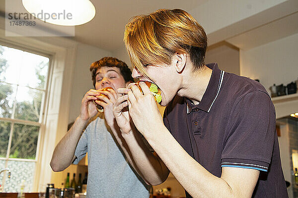 Hungrige Teenager essen Hamburger in der Küche