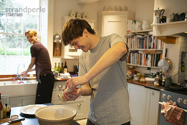 Glücklicher Teenager  der mit seinem Bruder in der Küche kocht