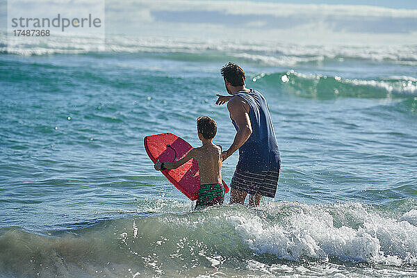 Vater und Sohn mit Bodyboard beim Beobachten der Meereswellen