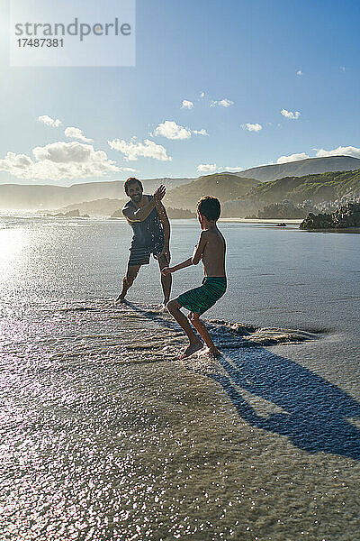 Verspielter Vater bespritzt Sohn am sonnigen Sommerstrand