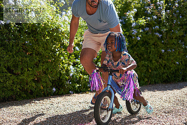Vater hilft seiner kleinen Tochter beim Fahrradfahren in einer sonnigen Einfahrt