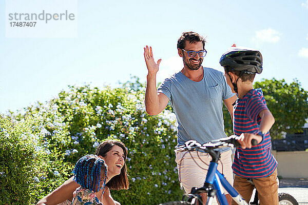 Glücklicher Vater und Sohn auf dem Fahrrad  die sich in der sonnigen Einfahrt die Hände reichen