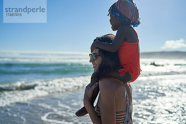 Mutter trägt süßes Kleinkind Tochter auf den Schultern auf Ozean Strand