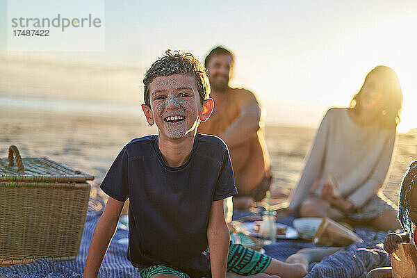 Portrait süßer Junge mit sandigem Gesicht am sonnigen Strand mit Familie