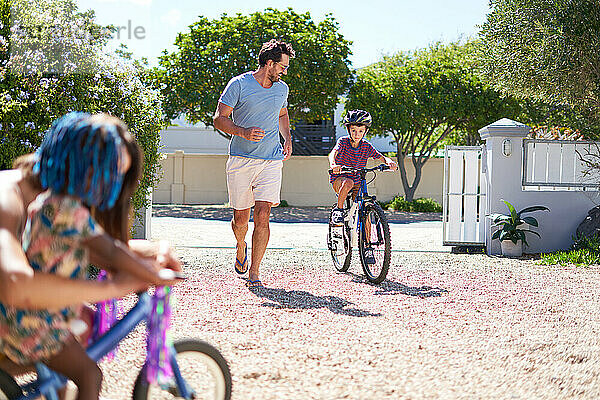 Vater und Sohn beim Laufen und Radfahren in einer sonnigen Einfahrt