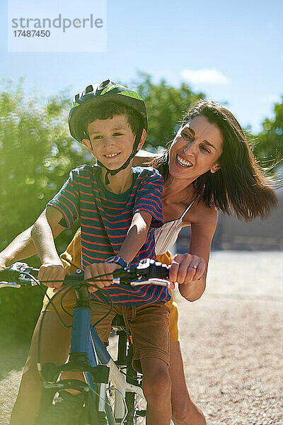 Glückliche Mutter mit Sohn beim Fahrradfahren in einer sonnigen Einfahrt