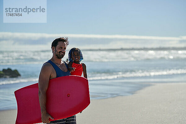 Glücklicher Vater und kleine Tochter mit Bodyboard am sonnigen Strand