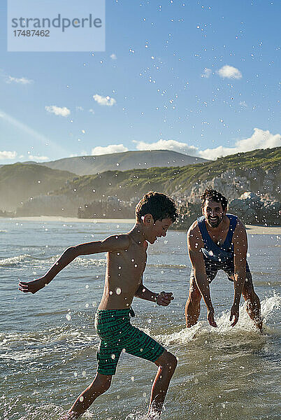 Glücklicher verspielter Vater plantscht mit seinem Sohn im sonnigen Sommermeer