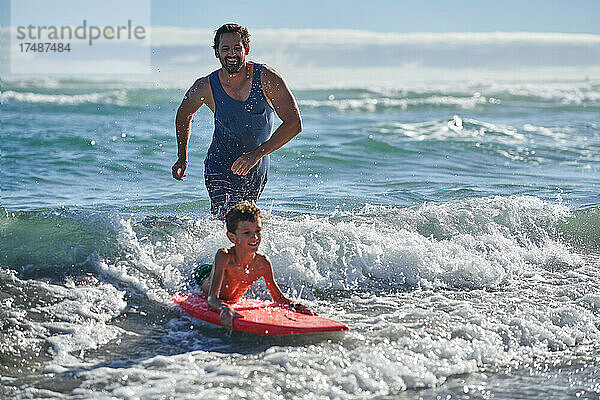 Glücklicher Vater und Sohn beim Bodyboarding in der sonnigen Meeresbrandung