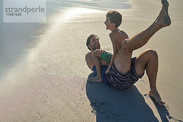 Glücklicher Vater und Sohn spielen am sonnigen Strand