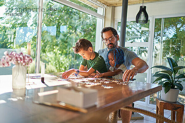Vater und Kinder beim Zusammensetzen eines Puzzles am Esstisch