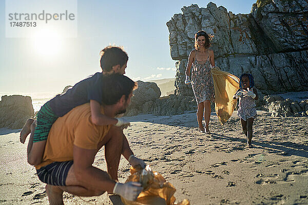 Glückliche Familie beim Müllsammeln am sonnigen Strand