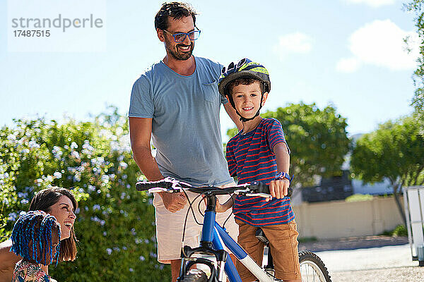 Porträt glücklicher Vater und Sohn auf Fahrrad in sonniger Einfahrt