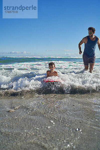 Vater und Sohn beim Bodyboarden in der sonnigen Meeresbrandung