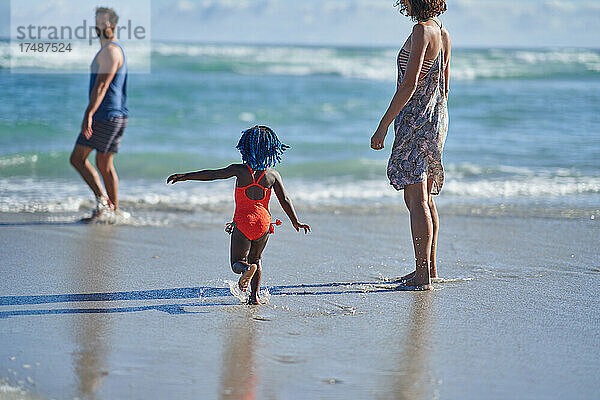 Nettes Kleinkind Mädchen spielen in sonnigen Ozean Brandung mit Eltern