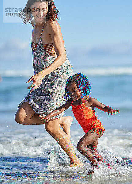 Glückliche Mutter und kleine Tochter laufen in der sonnigen Meeresbrandung