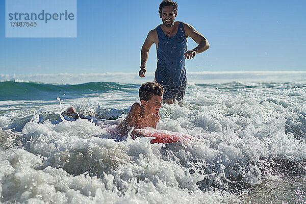 Glücklicher Vater und Sohn beim Bodyboarding in der sonnigen Meeresbrandung