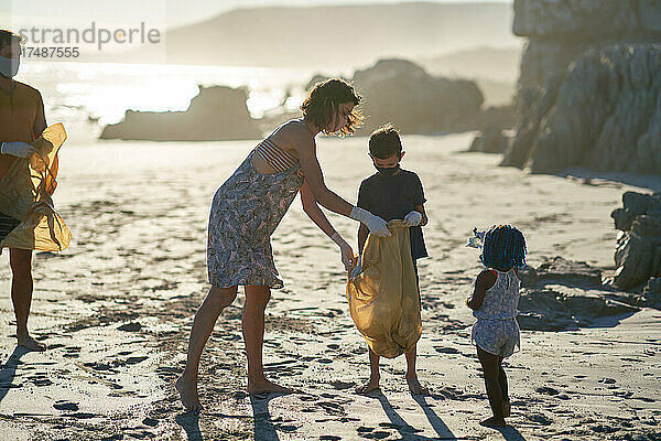 Familie mit Gesichtsmasken sammelt Müll am sonnigen Strand auf
