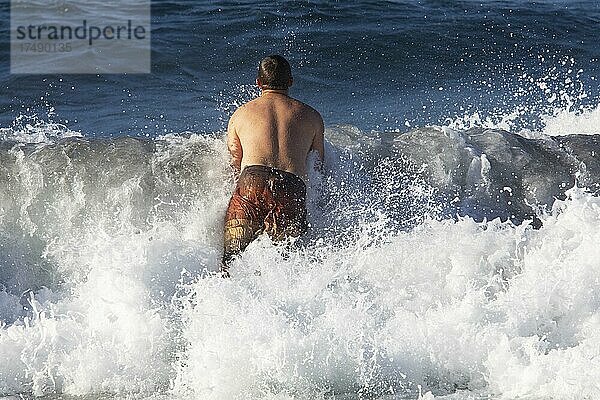 Junger Mann springt in eine hohe Welle am Strand von Praia de Santa Barbara  Ribeira Grande  Insel Sao Miguel  Azoren  Portugal  Europa
