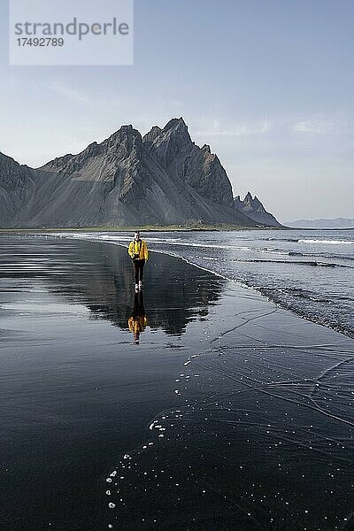 Junge Frau mit Regenjacke wandert an Strand  Schwarzer Lavastrand  Sandstrand  Landzunge Stokksnes  Austurland  Ostisland  Island  Europa