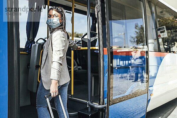 Junge Frau mit Gepäck und Schutzmaske beim Einsteigen in den Bus in Faro  Portugal  Europa