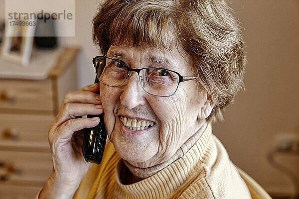 Seniorin zuhause lacht am Telefon  Köln  Nordrhein-Westfalen  Deutschland  Europa