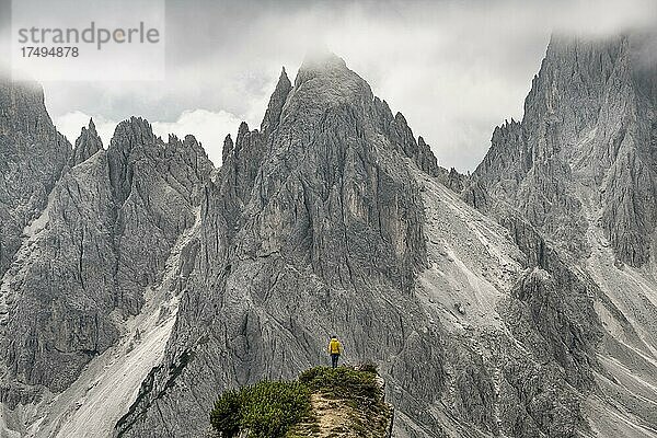 Wanderer steht auf einem Grat  hinten Berggipfel und spitze Felsen  dramatischer Wolkenhimmel  Cimon di Croda Liscia und Cadini-Gruppe  Auronzo di Cadore  Belluno  Italien  Europa