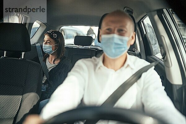 Taxifahrer in einer Maske mit einer weiblichen Kundin auf dem Rücksitz mit Maske