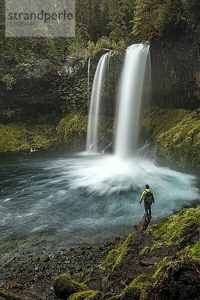 Junger Mann steht auf einem Stein  Wasserfall in dichter Vegetation  Koosah Falls  Oregon  USA  Nordamerika
