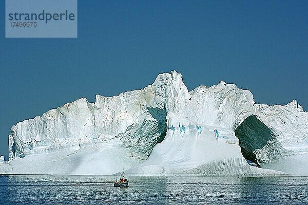 Kleines Fischerboot vor riesigem Eisberg mit zwei großen Höhlen  Diskobucht  Ilulissat  Grönland  Dänemark  Nordamerika