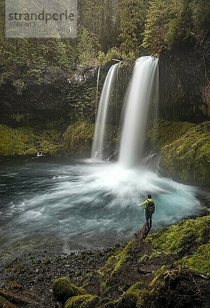 Junger Mann steht auf einem Stein  Wasserfall in dichter Vegetation  Koosah Falls  Oregon  USA  Nordamerika