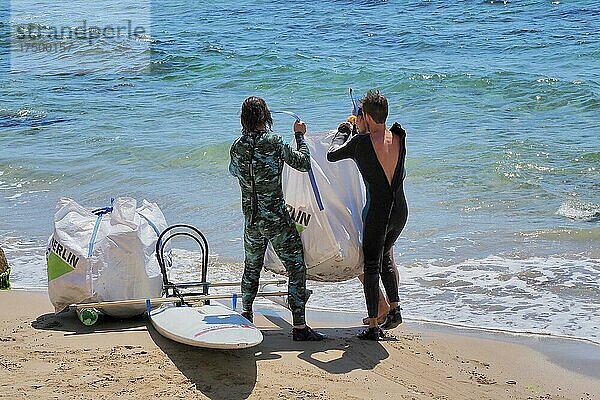Zwei Männer im Taucheranzug hieven schweren Sack mit Plastikabfall auf ein Transport-Board  Beachcleaning  Almeria  Andalusien  Spanien  Europa