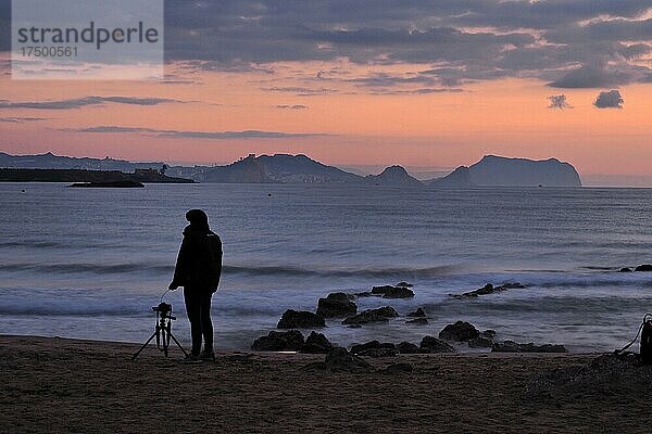 Fotograf mit Kamera und Stativ morgens am Meer  Morgenstimmung am Meer mit fotografierender Frau  Sonnenaufgang am Strand mit Blick auf Aguilas und Cabo Cope  Murcia  Spanien  Europa